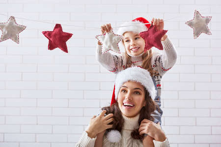 Merry Christmas! Happy mother and daughter hang a Christmas garland.の写真素材
