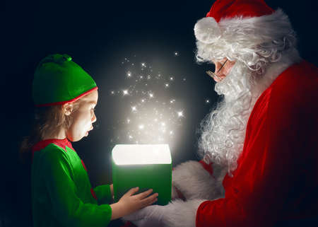 Cute little girl and Santa Claus opening a magic gift box.