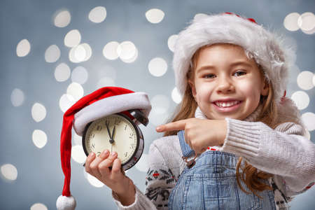 Christmas Eve! Cheerful child in a Christmas hat with alarm clockの写真素材