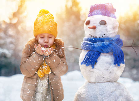 happy child girl plaing with a snowman on a snowy winter walkの写真素材