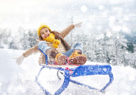 Child sledding. Little girl enjoying a sleigh ride. Child girl riding a sledge. Child plays outdoors in snow. Outdoor fun for family winter vacation.の写真素材