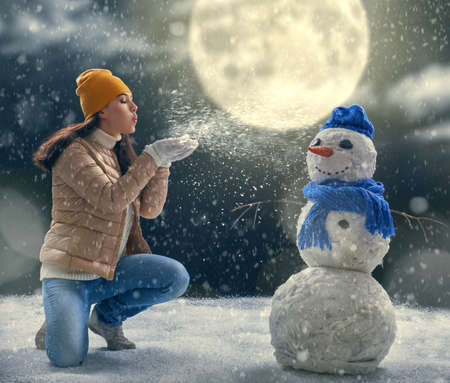 happy young woman plaing with a snowman on a snowy winter walk. Beautiful girl enjoys the game. Girl playing outdoors in snow. Outdoor fun for winter vacation.の写真素材