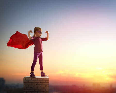 Little child girl plays superhero. Child on the background of sunset sky. Girl power concept