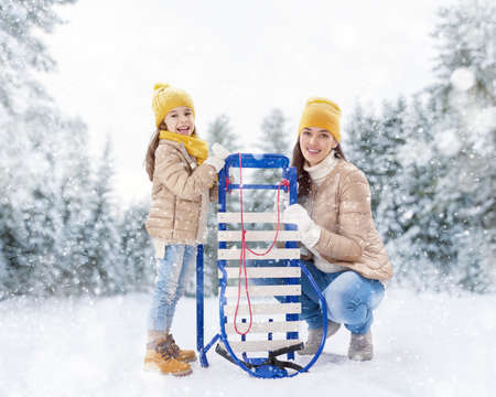 Child girl and mother sledding. Family plays outdoors in snow. Outdoor fun for family winter vacation.の写真素材