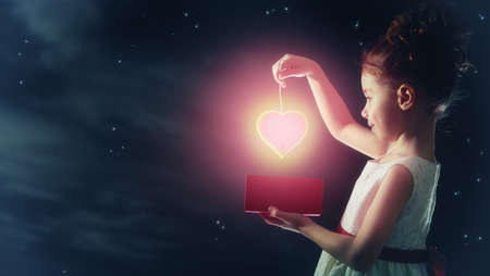Sweet child girl with red heart. Happy little girl with gift box on background of star sky. Wedding,...