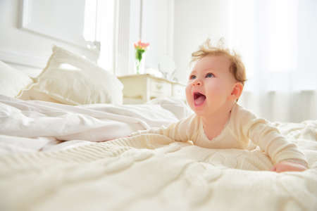 Beautiful smiling cute baby girl on the bed in the room. Happy child laughing.