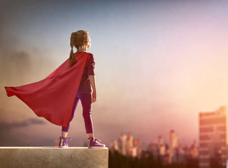 Little child girl plays superhero. Child on the background of sunset sky. Girl power concept