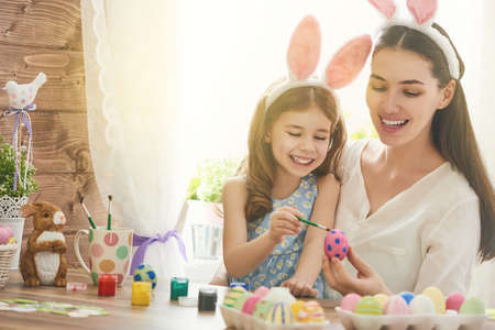 Happy easter! A mother and her daughter painting Easter eggs. Happy family preparing for Easter. Cute little child girl wearing bunny ears on Easter day.の写真素材