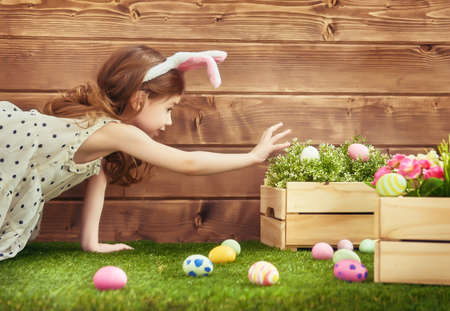 Happy Easter! Cute little child girl wearing bunny ears on Easter day. Girl hunts for Easter eggs on...