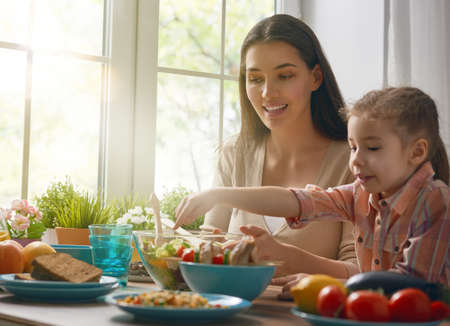 Happy family having dinner together sitting at the rustic wooden table. Mother and her daughter enjoying family dinner together.の写真素材