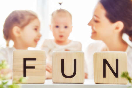 Happy loving family playing with blocks and having fun. Blocks have letters. Mother and her daughters lay out cubes and word fun.の写真素材