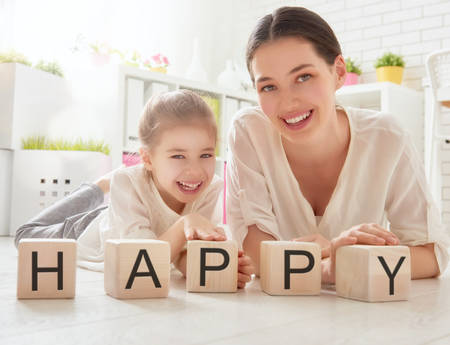 Happy loving family playing with blocks and having fun. Blocks have letters. Mother and her daughter lay out cubes and word happy.の写真素材