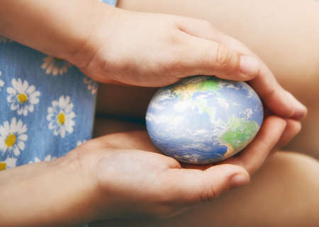 children's hands holding an Easter egg. the egg has a picture of the globe. the concept of peace and care about the environmentの写真素材
