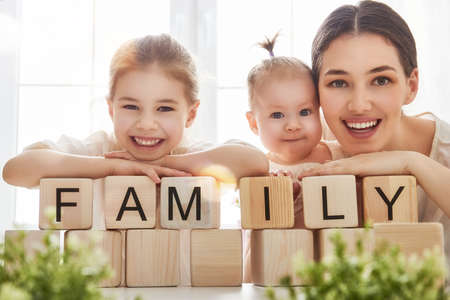 Happy loving family playing with blocks and having fun. Blocks have letters. Mother and her daughters lay out cubes and word family.の写真素材