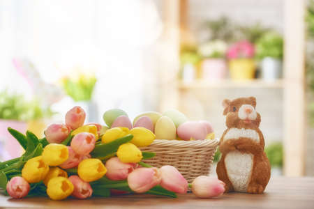 Happy Easter! Easter background with colorful eggs in basket, yellow and pink tulips and rabbit....