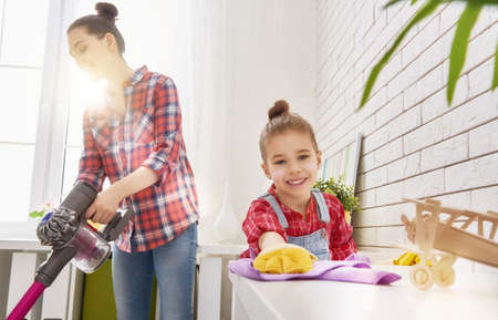 Happy family cleans the room. Mother and daughter do the cleaning in the house. A young woman and a little child girl wiped the dust and vacuumed the floor.の写真素材