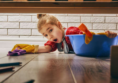Charming little helper. Cute little child girl makes cleaning the house. Girl wipes the floor.の写真素材