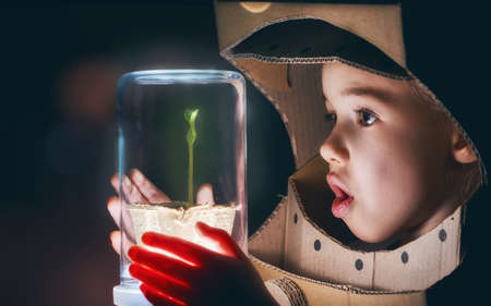 Child is dressed in an astronaut costume. Child sees a sprout in a glass case. The concept of environmental protection.の写真素材