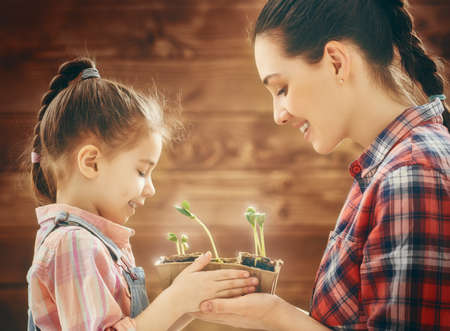 Cute child girl helps her mother to care for plants. Happy family engaged in gardening in the backyard. Mother and her daughter watch as a growing sprout. Spring concept, nature and care.の写真素材