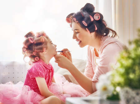 Happy loving family. Mother and daughter are doing hair and having fun. Mother putting lipstick on her daughter.