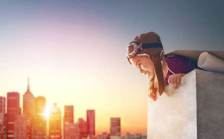 Little child girl plays astronaut. Child on the background of sunset sky. Child in an astronaut costume plays and dreams of becoming a spaceman.の写真素材