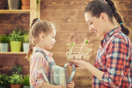 Cute child girl helps her mother to care for plants. Happy family engaged in gardening in the backyard. Mother and her daughter watering a growing sprout. Spring concept, nature and care.の写真素材