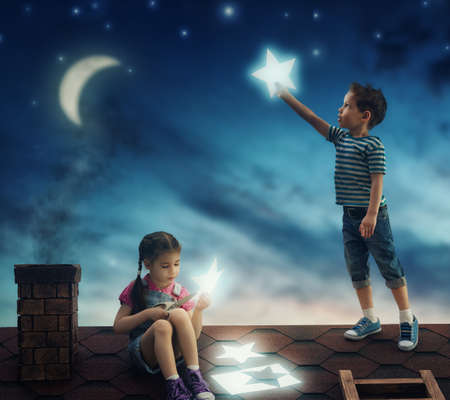Fairy tale! The children hung the stars in the sky. Boy and girl on the roof cut out stars.の写真素材