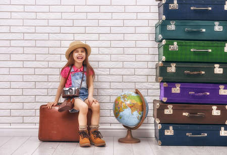 happy child girl against a white brick wall. girl having suitcases and dreaming of traveling.の写真素材