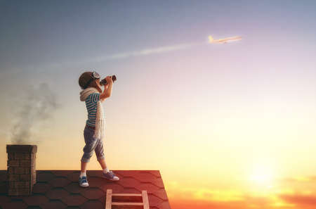 Cute little child playing on the roof of the house and looking at the sky and dreaming of becoming a pilots.の写真素材