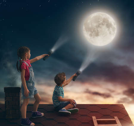 Two cute children sit on the roof and look at the moon.の写真素材