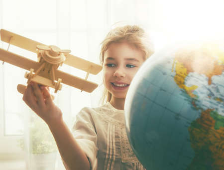 Go on an adventure! Cute child girl playing with toy airplane and globe.の写真素材