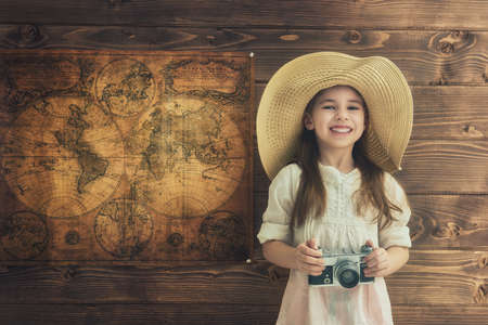 Go on an adventure! Cute child girl with vintage camera on wooden background wall and maps.の写真素材