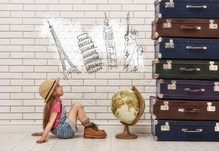 happy child girl against a white brick wall. girl having suitcases and dreaming of traveling.の写真素材