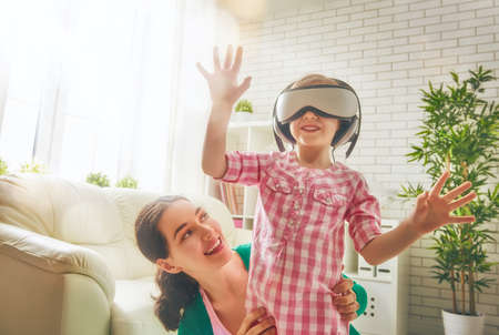 Happy family! Mother and her child daughter play game in virtual reality glasses.の写真素材