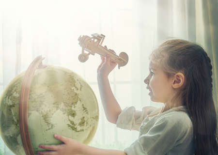 Go on an adventure! Cute child girl playing with toy airplane and globe.の写真素材
