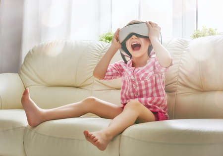 Cute little child girl playing game in virtual reality glasses.