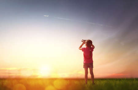 Cute little child girl looking through binoculars to the sky and flying plane.の写真素材