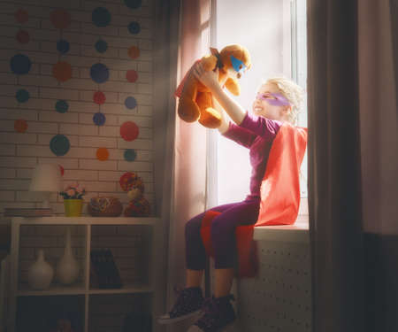 Little child girl plays superhero. Child plays with her friend a Teddy bear. Girl power concept.の写真素材