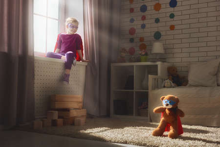 Little child girl plays superhero. Child plays with her friend a Teddy bear. Girl power concept.の写真素材