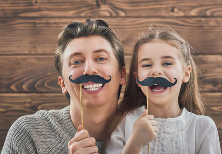 Funny family! Father and his child daughter girl with a paper accessories. Beauty funny girl holding paper mustache on stick. Beautiful young man holding paper mustache on stick.の写真素材