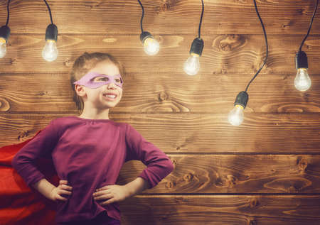 Little child girl plays superhero. Child on the background of wooden wall. Girl power concept.の写真素材