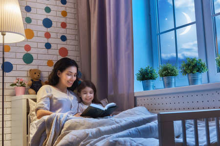 Family reading bedtime. Pretty young mother reading a book to her daughter.の写真素材