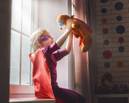 Little child girl plays superhero. Child plays with her friend a Teddy bear. Girl power concept.の写真素材