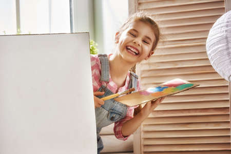 Happy little child draws paints. Sweet girl engaged in creativity.の写真素材