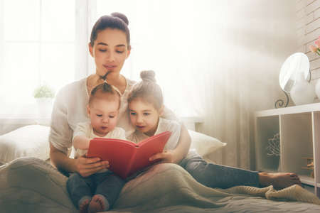 happy loving family. pretty young mother reading a book to her daughtersの写真素材