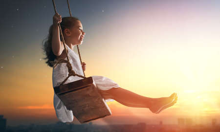 Happy laughing child girl on swing in sunset summerの写真素材
