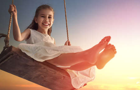 Happy laughing child girl on swing in sunset summerの写真素材