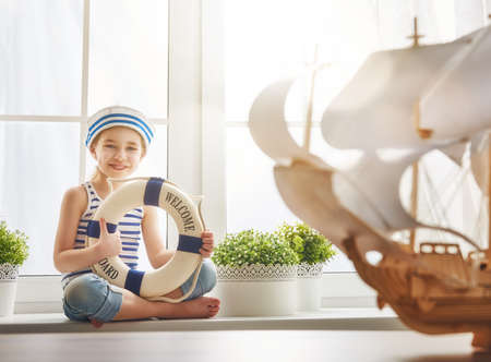 Adorable little child girl looks at toy ship and dreams of sea, adventures and travel.の写真素材