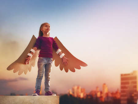 Little girl plays outdoors. Child on the background of sunset sky. Kid with the wings of a bird dreams of flying.の写真素材