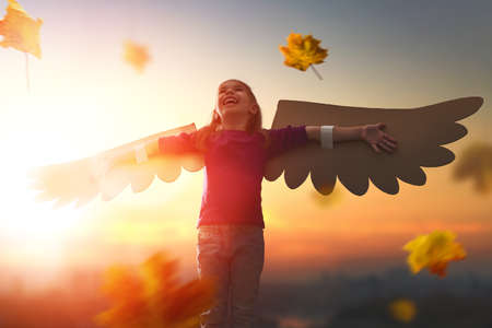 Little girl plays outdoors. Child on the background of sunset sky. Kid with the wings of a bird dreams of flying.の写真素材